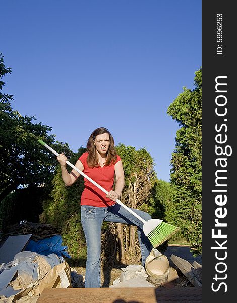 Woman looking angry as she goes through a pile of garbage with a broom. Vertically framed photo. Woman looking angry as she goes through a pile of garbage with a broom. Vertically framed photo.