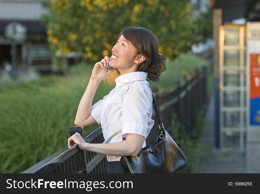 Smiling woman talking on cellphone while leaning over railing. Horizontally framed photo. Smiling woman talking on cellphone while leaning over railing. Horizontally framed photo.