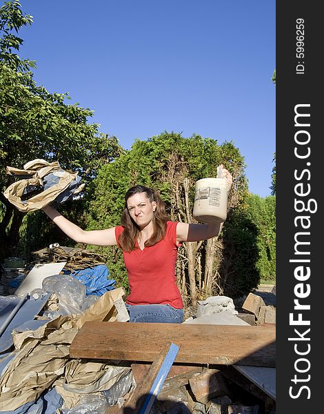 Woman looking frustrated as she stands in a pile of rubble and holds up garbage. Vertically framed photograph. Woman looking frustrated as she stands in a pile of rubble and holds up garbage. Vertically framed photograph
