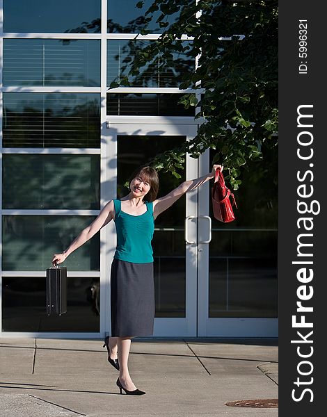 Woman smiles at camera while holding briefcase and red handbag out to her side. She is kicking up one leg. Vertically framed photo. Woman smiles at camera while holding briefcase and red handbag out to her side. She is kicking up one leg. Vertically framed photo.
