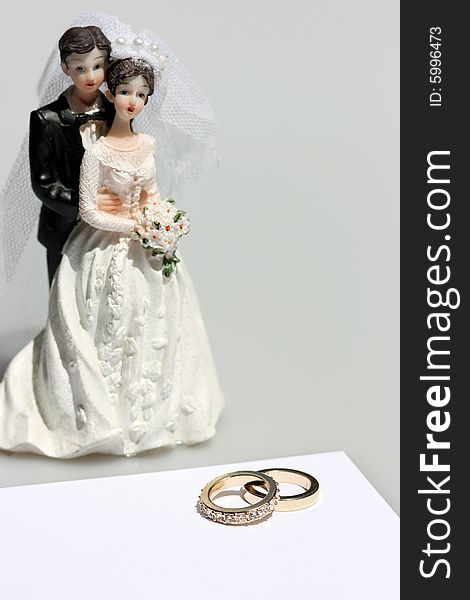 Figurine of bride and groom with wedding bands and a blank card. Figurine of bride and groom with wedding bands and a blank card