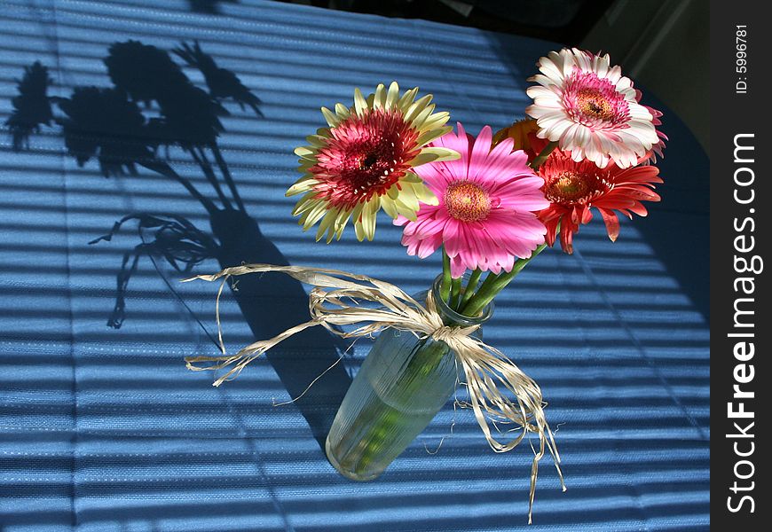 A vase of colorful flowers on a blue table with shadows. A vase of colorful flowers on a blue table with shadows