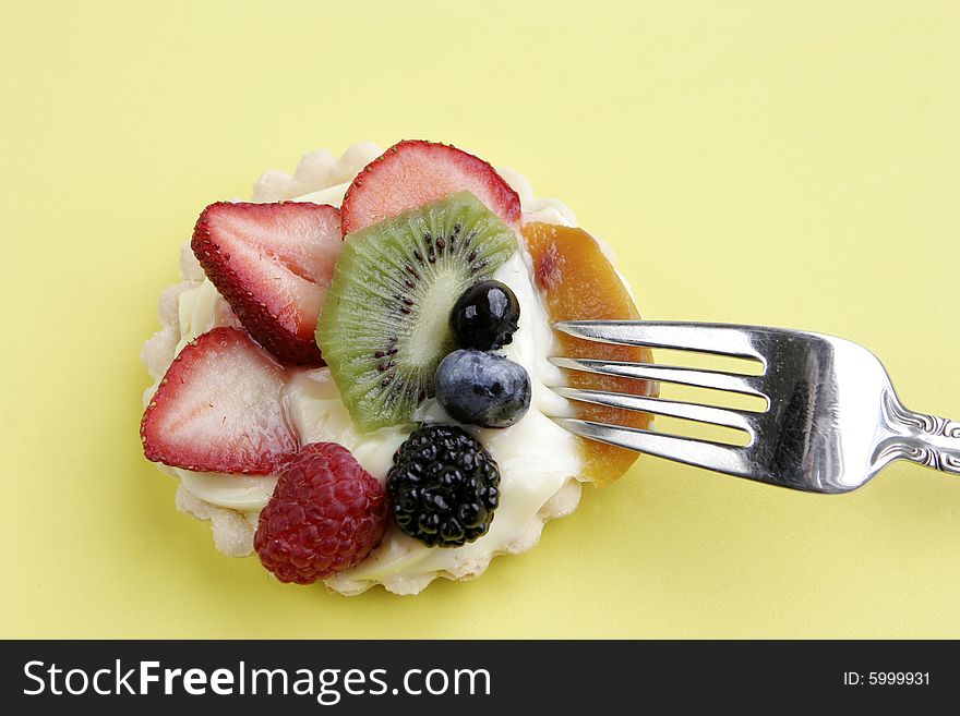 Cream-filled pastry tart topped with an assortment of juicy berries, kiwi, and peach. A silver fork stands ready to enjoy the gourmet treat. Cream-filled pastry tart topped with an assortment of juicy berries, kiwi, and peach. A silver fork stands ready to enjoy the gourmet treat.