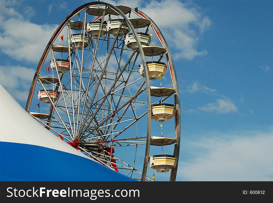 Ferris wheel with tent in the foreground. There is a blue sky with wisps of clouds. Ferris wheel with tent in the foreground. There is a blue sky with wisps of clouds.