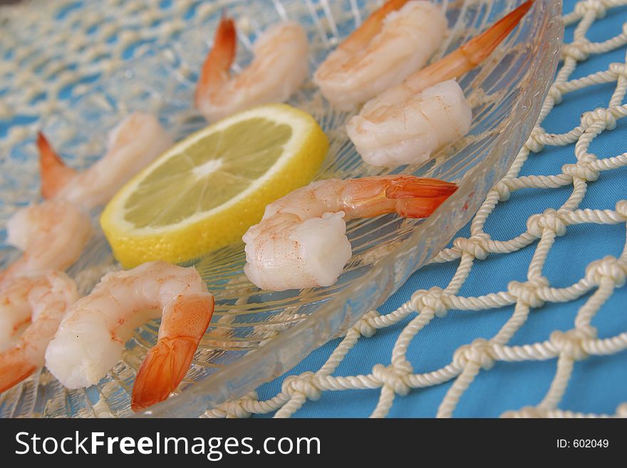 Boiled shrimp and lemon slice on clear plate with blue tablecloth and netting. Boiled shrimp and lemon slice on clear plate with blue tablecloth and netting.