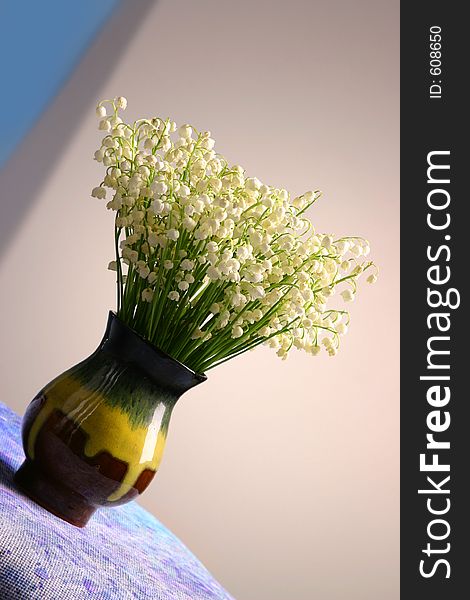 A vase with forest flowers of lilies on the valley standing on the inclined surface. A vase with forest flowers of lilies on the valley standing on the inclined surface