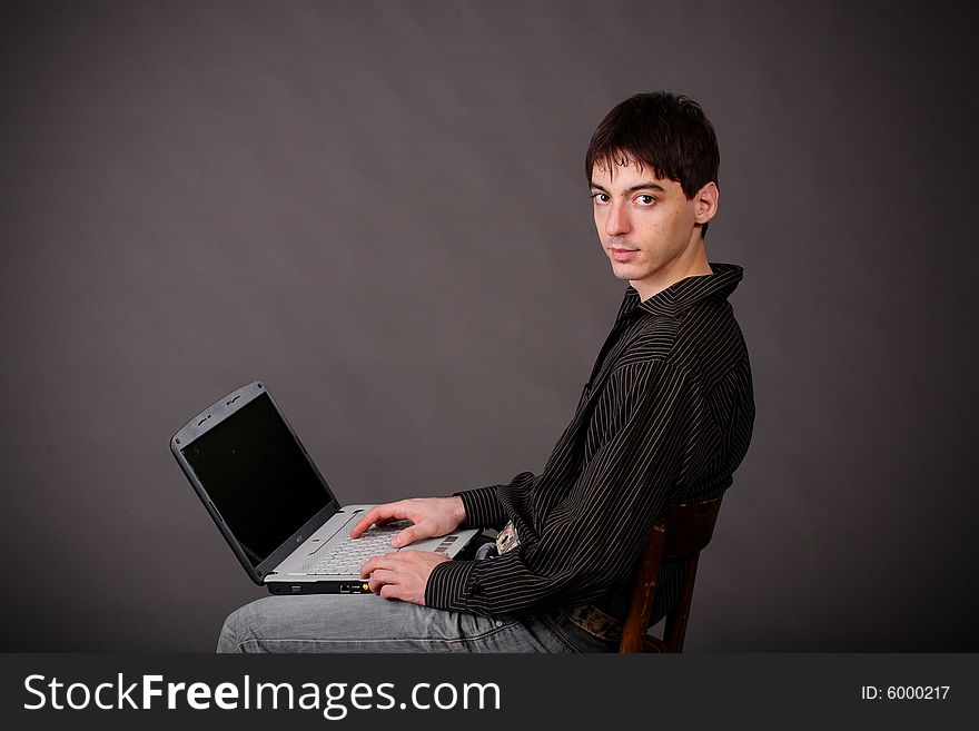 Casual young man sitting with laptop/ Dark bakground