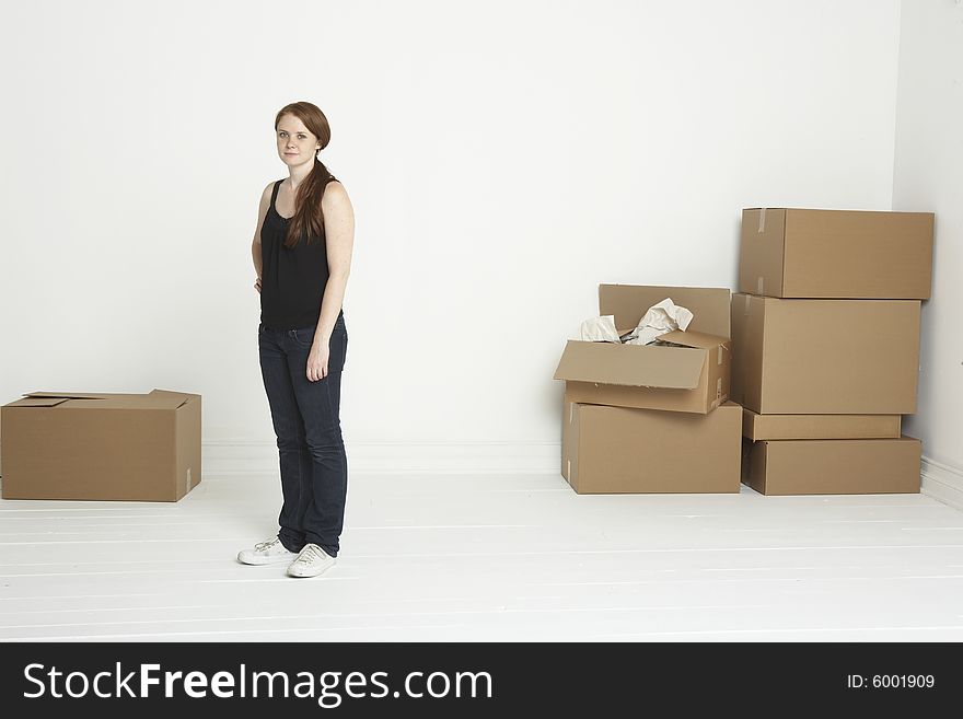Young red headed woman standing in white room with moving boxes to both sides. Young red headed woman standing in white room with moving boxes to both sides.