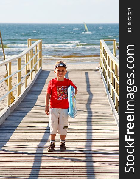 Little boy with a buoy on a bridge walking towards a beach