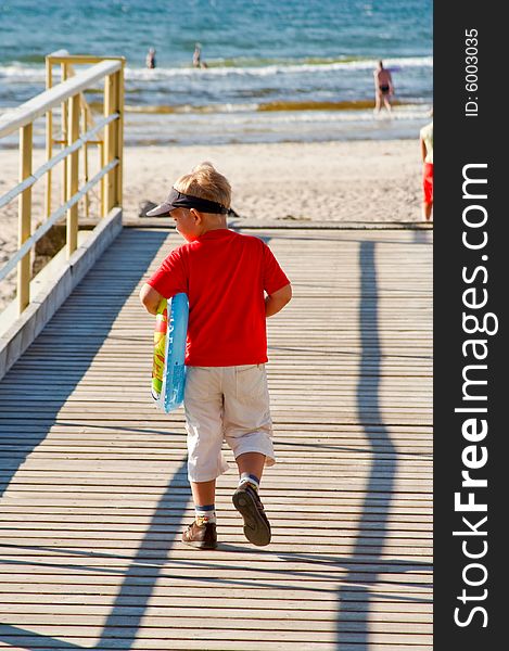 Little boy with a buoy on a bridge walking towards a beach. Little boy with a buoy on a bridge walking towards a beach