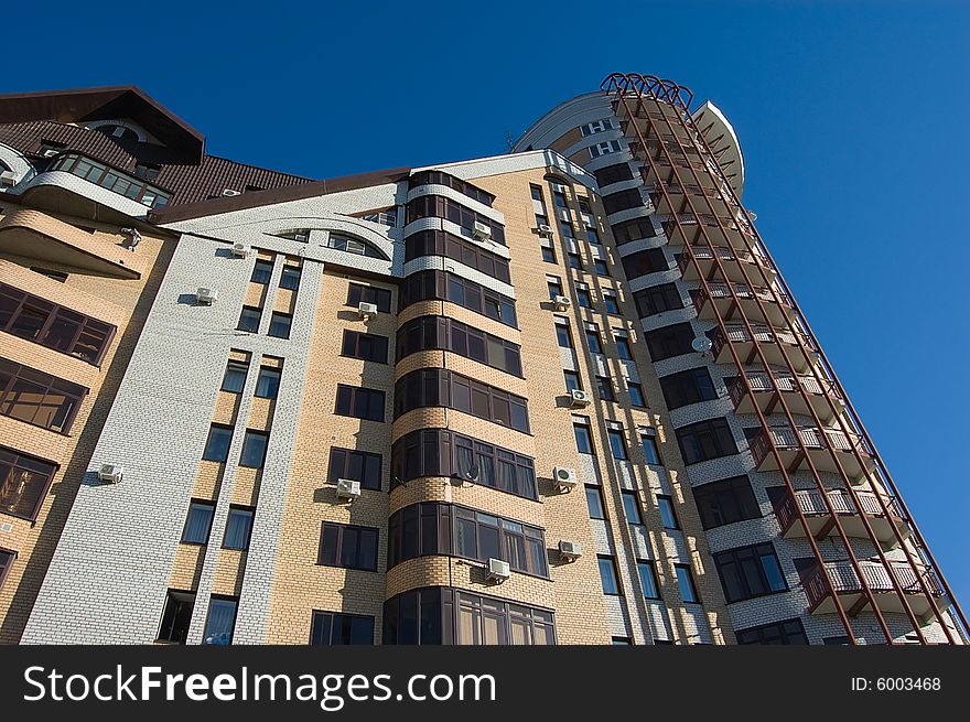 New modern brick multistory house on deep blue sky background in three colors: red, yellow, grey.