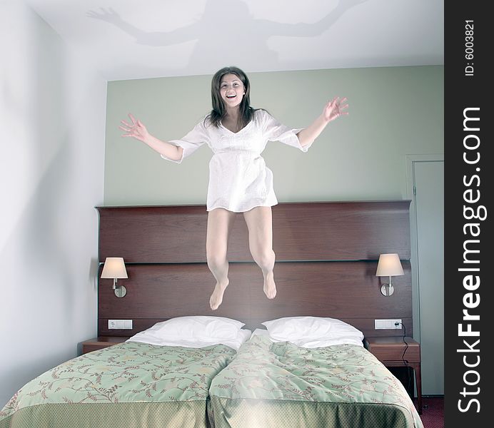 Happy young girl jumping on bed in hotel room, selective focus on face, hands and legs motion blurred. Happy young girl jumping on bed in hotel room, selective focus on face, hands and legs motion blurred