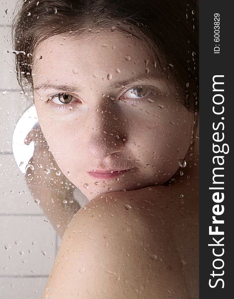 Young woman looking through the cabin shower glass with water drops on it. Young woman looking through the cabin shower glass with water drops on it