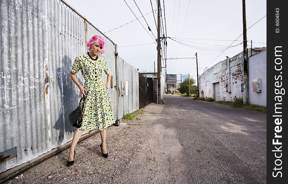 Woman with pink hair wearing polka dot dress in alley with purse. Woman with pink hair wearing polka dot dress in alley with purse