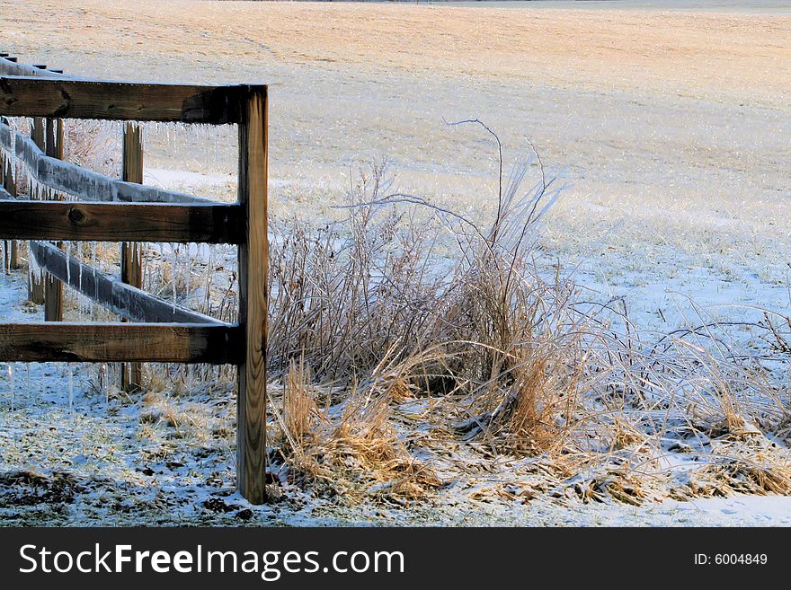 Icicles on a wood fence and an icy field and weeds. Icicles on a wood fence and an icy field and weeds