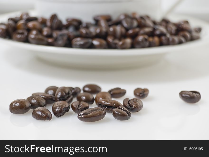 Closeup shot of coffee beans in front of cup, shot against white background