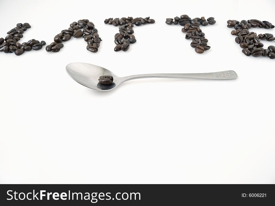 Word latte spelled with coffee beans; focus is on spoon and bean at foreground; copy space below