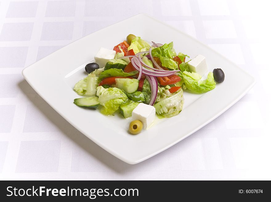 Greek Salad with vegetables, herbs and feta cheese on white plate