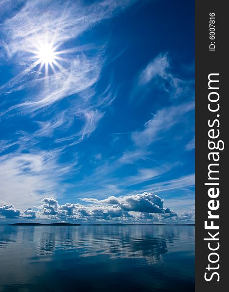 Rays of sun on bright blue sky with fluffy clouds with reflection on lake. Srednee Kuyto Lake, Karelia, Russia. Rays of sun on bright blue sky with fluffy clouds with reflection on lake. Srednee Kuyto Lake, Karelia, Russia