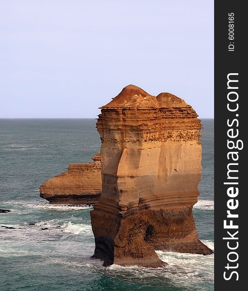 Large cliff remnant in ocean with visible layering of rock and green ocean. Large cliff remnant in ocean with visible layering of rock and green ocean