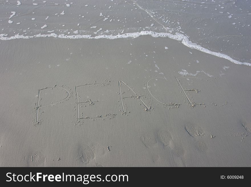 The word peace written in the sand with the water advancing on it.