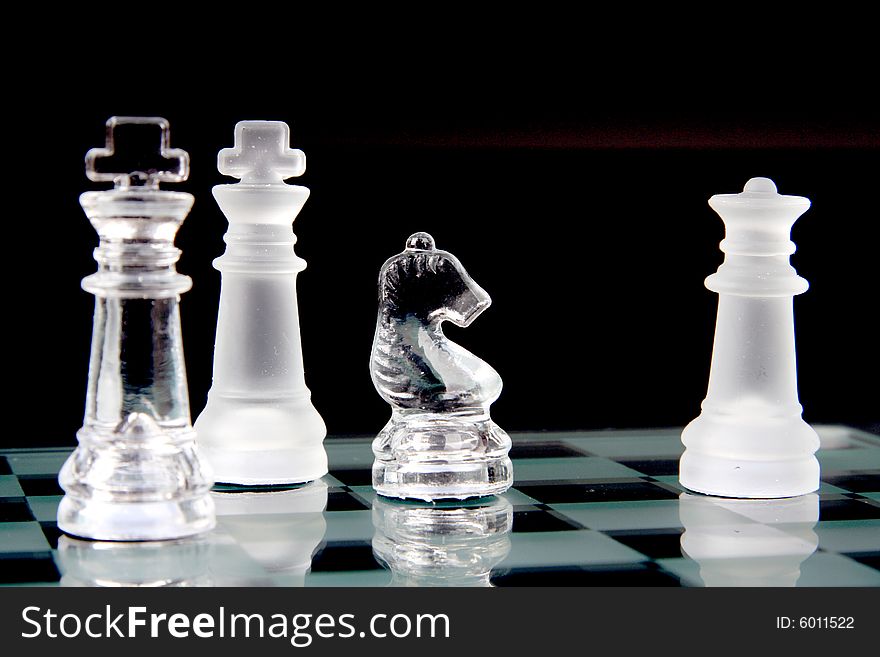 Glass chessmen on a chessboard over black background