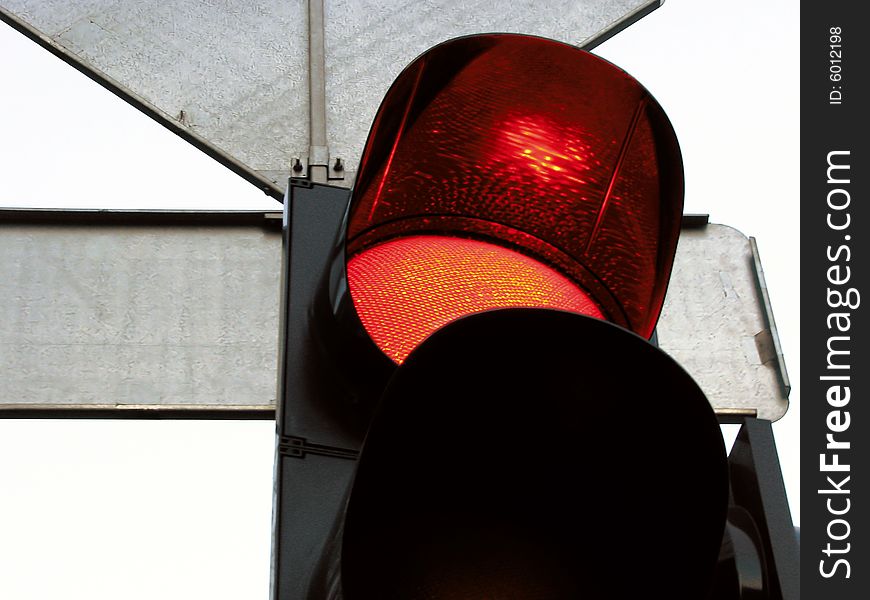 Red signal under a cap of a traffic light and a back of traffic signs. Red signal under a cap of a traffic light and a back of traffic signs