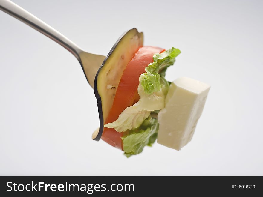 Lettuce, cheese, tomato, zucchini, meat carving with a fork isolated over white