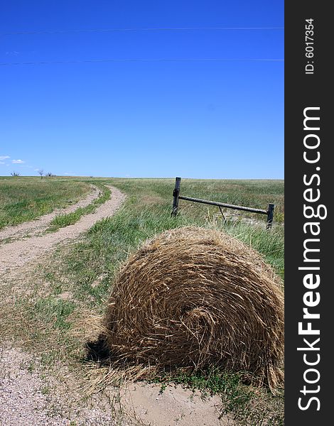 Cylindrical staw bale lies next to a field road and gate. Cylindrical staw bale lies next to a field road and gate