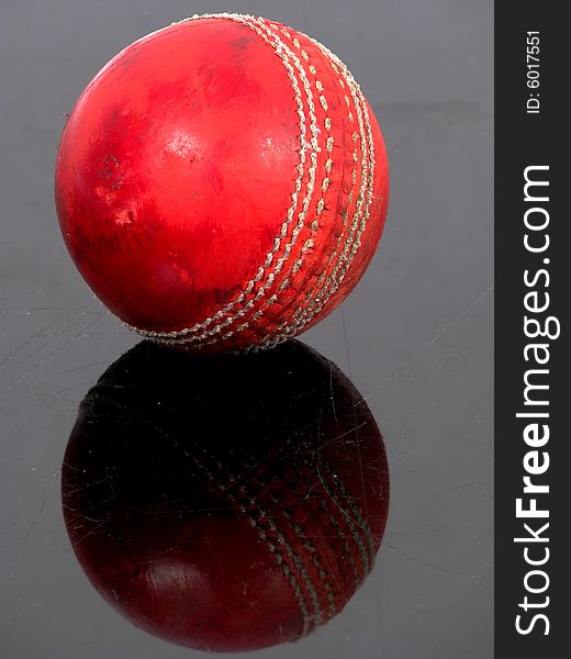 Red cricket ball on a black shiny surface. Red cricket ball on a black shiny surface