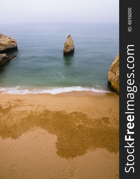 Empty beach with a rock in the middle of the bay.