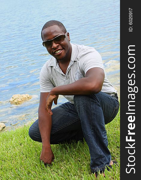 Young stylish male squatting near a pond. Young stylish male squatting near a pond