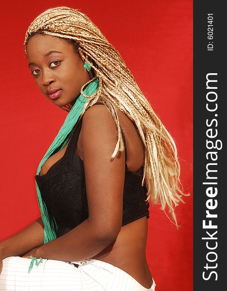 An busty young Jamaican girl in a black top and white pants, long blond hair sitting on a bar chair in an studio for red background. An busty young Jamaican girl in a black top and white pants, long blond hair sitting on a bar chair in an studio for red background.