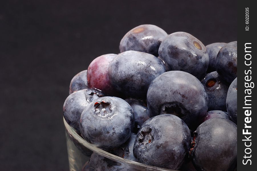 Blueberries in a glass bowl against a black background