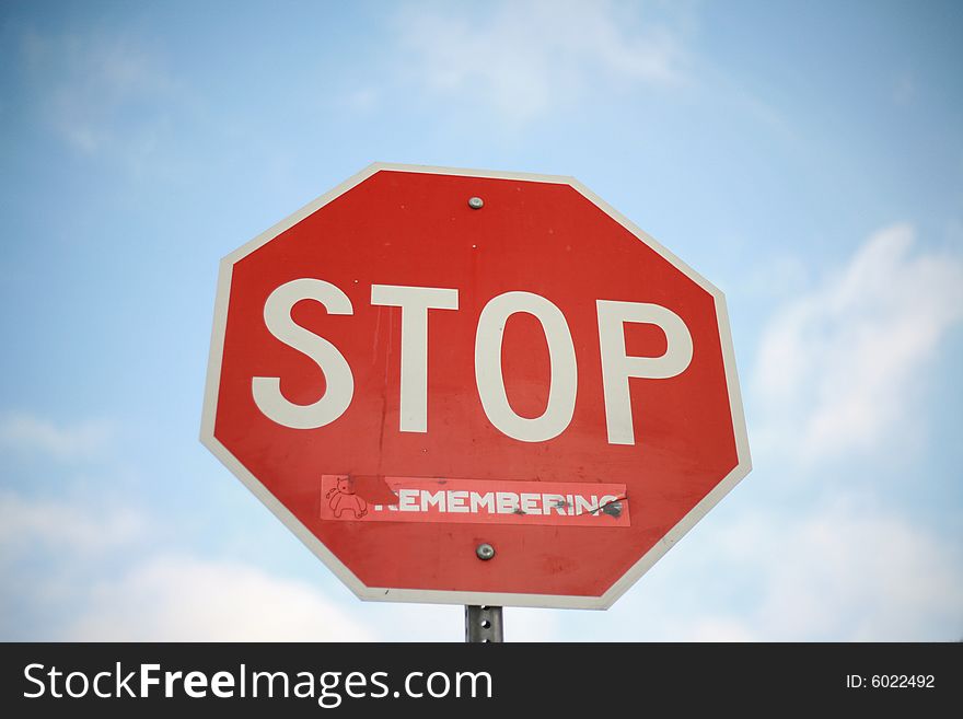 Stop sign with sticker against blue sky with clouds