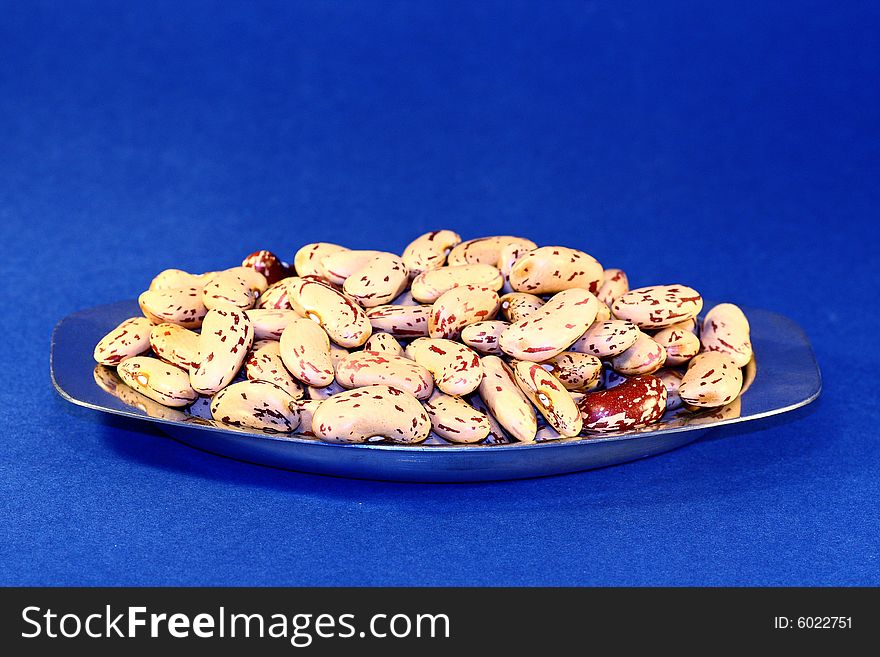 Bunch of piled pinto beans on a plate isolated on a blue background. Bunch of piled pinto beans on a plate isolated on a blue background.