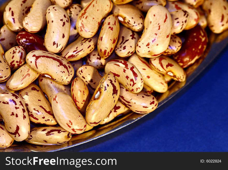 Bunch of pinto beans piled on a plate isolated on a blue background. Bunch of pinto beans piled on a plate isolated on a blue background.