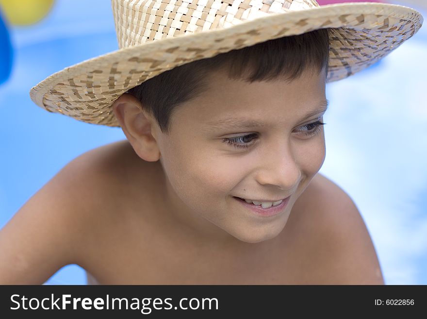 Young boy sits on the side of a swimming pool with hat. Young boy sits on the side of a swimming pool with hat