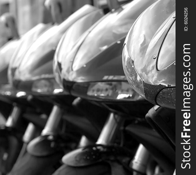 6 black motorbikes parked in a row, focus is on the front bike. 6 black motorbikes parked in a row, focus is on the front bike