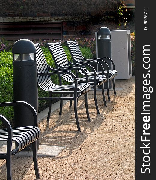 Row of black metal armchairs on sand ground