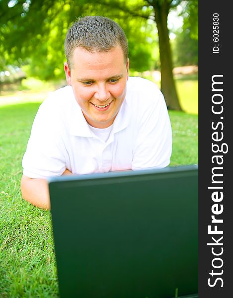 Handsome caucasian man using computer outdoor in grassy park. Handsome caucasian man using computer outdoor in grassy park