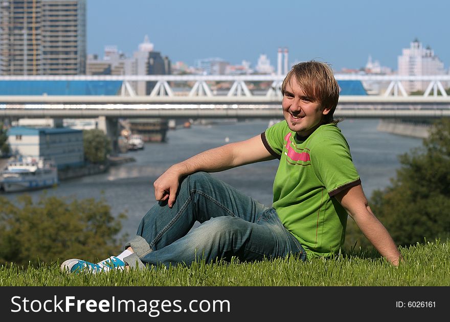 Happy young man sitting on the grass at river side