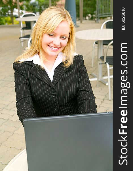 Smiling and happy blond business woman using laptop in modern cafe setting. Smiling and happy blond business woman using laptop in modern cafe setting