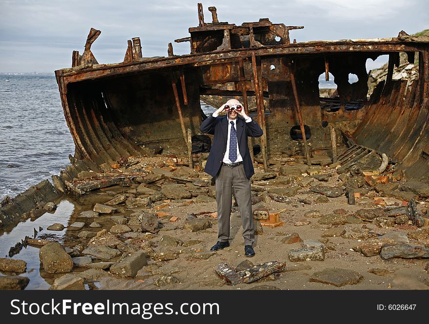 Businessman in the rusting hull of shipwreck, with binoculars looking out to the horizon, asking the question is their an escape from a sinking business. Businessman in the rusting hull of shipwreck, with binoculars looking out to the horizon, asking the question is their an escape from a sinking business