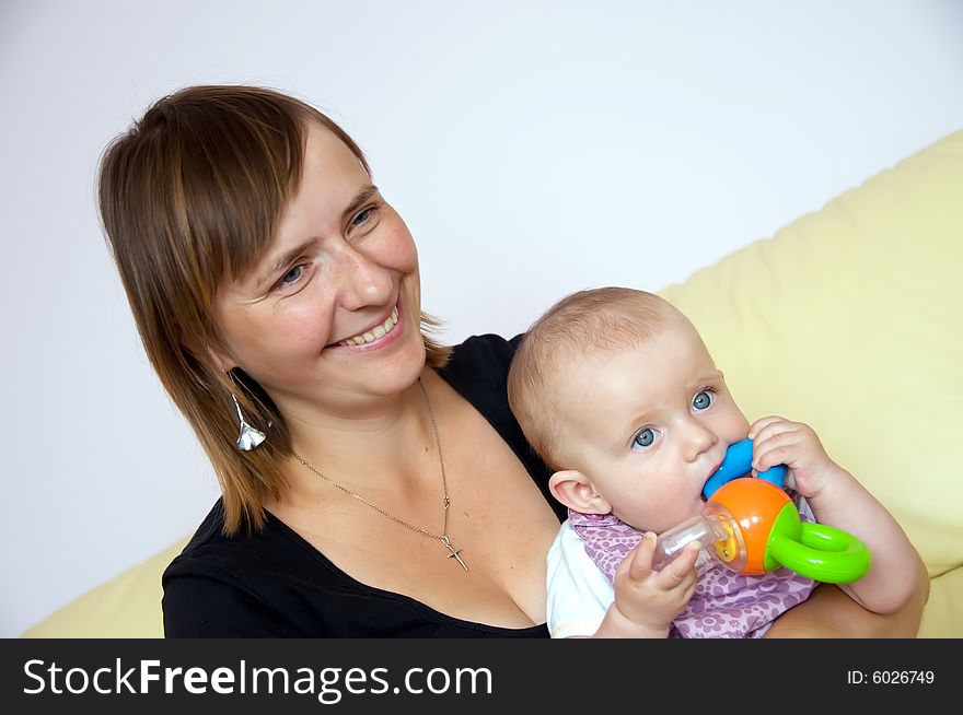 Happy mother with baby in her arms sitting on sofa. Baby is playing with a toy. Happy mother with baby in her arms sitting on sofa. Baby is playing with a toy.