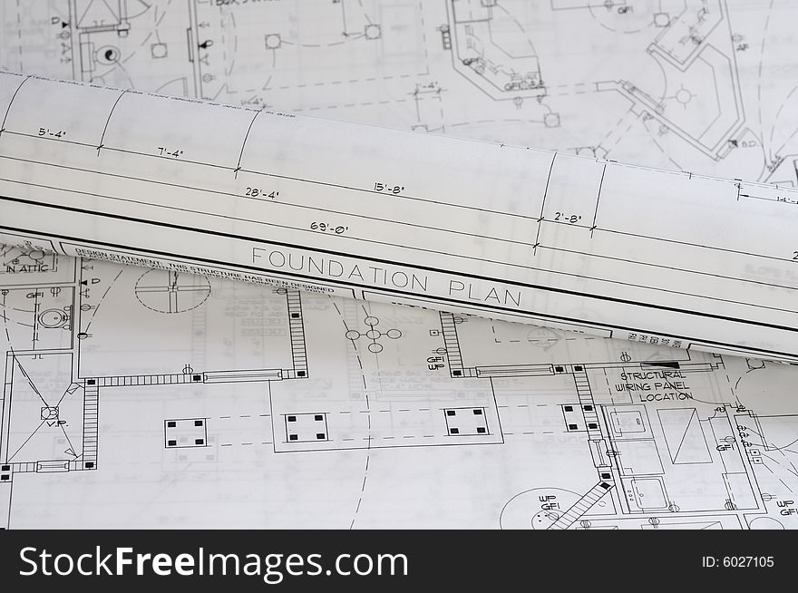 A crisp white blueprint rolled up on top of a foundation plan. A crisp white blueprint rolled up on top of a foundation plan.