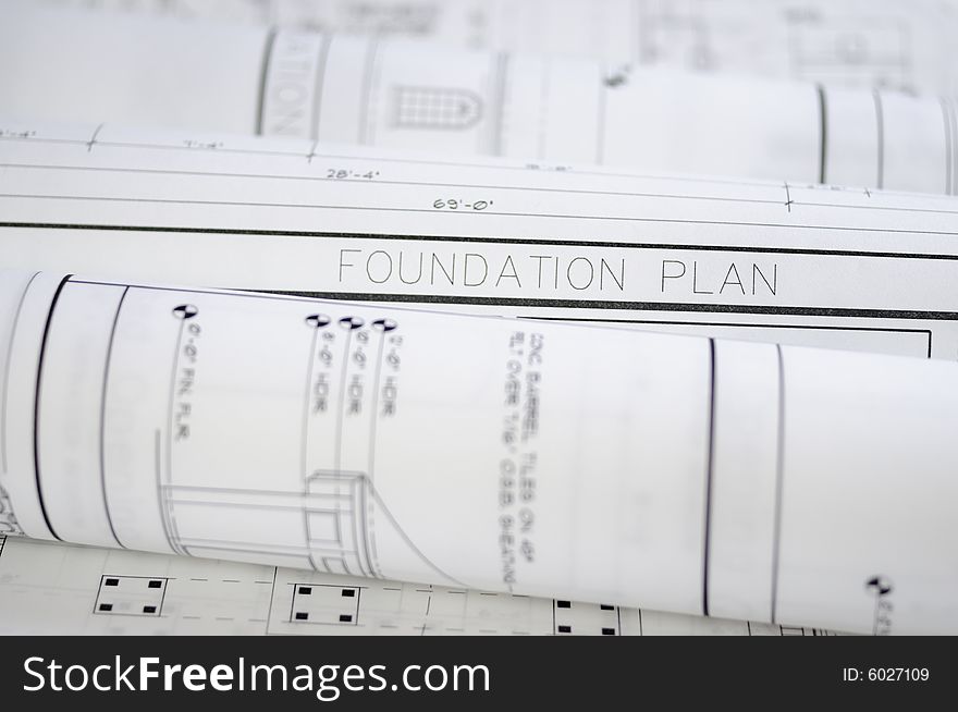 Crisp white blueprints rolled up on top of a foundation plan.