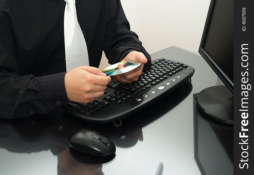 Businessman sitting on the desk, holding a disc, in front of a computer. Businessman sitting on the desk, holding a disc, in front of a computer