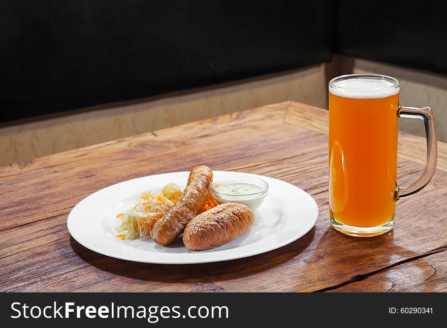 Fresh sausages with vegetables and mug with beer on a plate closeup