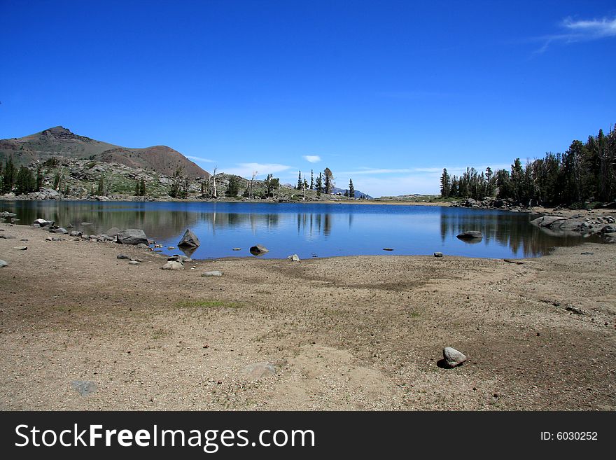 Image of low level of water in a small mountain lake, against a very blue sky. Image of low level of water in a small mountain lake, against a very blue sky.